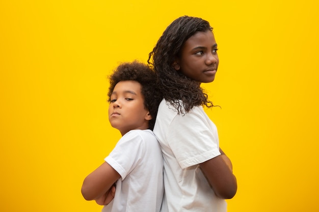 Infeliz hermano y hermana. Hermanos jóvenes de pie espalda con espalda con los brazos cruzados sobre amarillo.