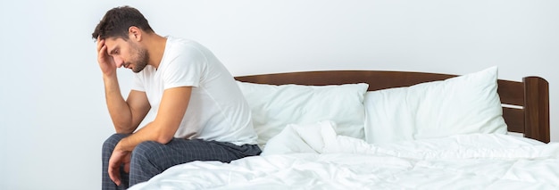 El infeliz hombre sentado en la cama sobre el fondo blanco.