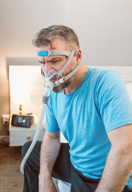 Infeliz hombre sorprendido con problemas respiratorios crónicos sorprendido por el uso de la máquina cpap sentado en la cama