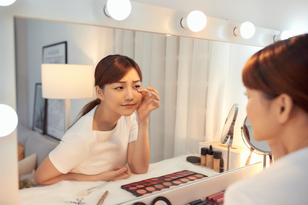 Infeliz jovem asiática na frente de um espelho olhando suas rugas
