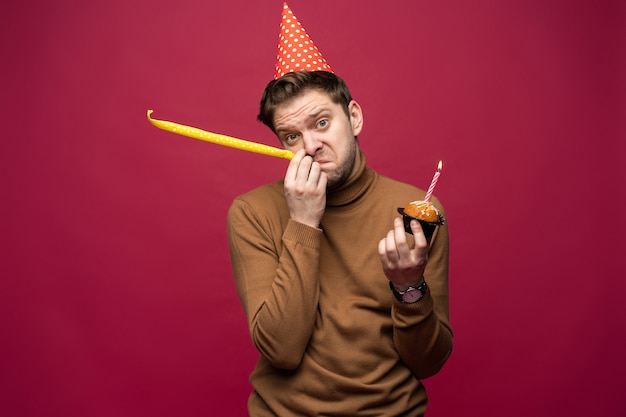 Infeliz joven estresado con cupcake de cumpleaños con mirada infeliz