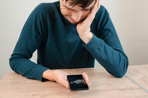 Infeliz joven mirando su teléfono inteligente con una pantalla rota