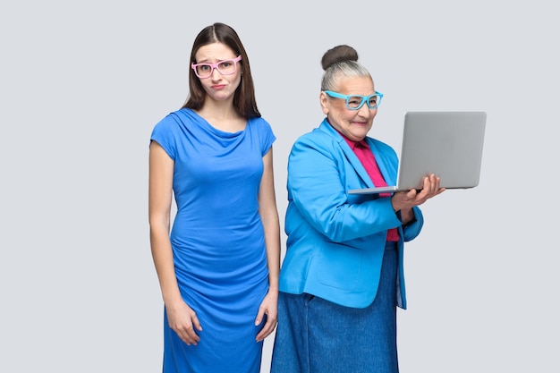 Foto infeliz joven de pie cerca de la felicidad computadora de trabajo de mujer mayor