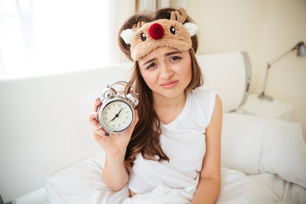 Infeliz mujer sosteniendo despertador en la cama