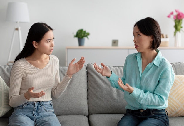 Infeliz mulher asiática madura e sua filha adulta brigando discutindo entre si no sofá em
