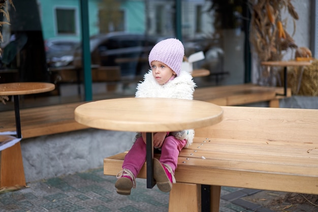 Infeliz niña sentada en un café al aire libre en la mesa de la temporada de otoño niña caucásica losy en la ciudad sentado triste solitario