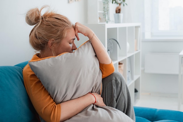 Infeliz solitaria mujer deprimida en casa ella sentada sofá escondiendo su cara almohada concepto de depresión