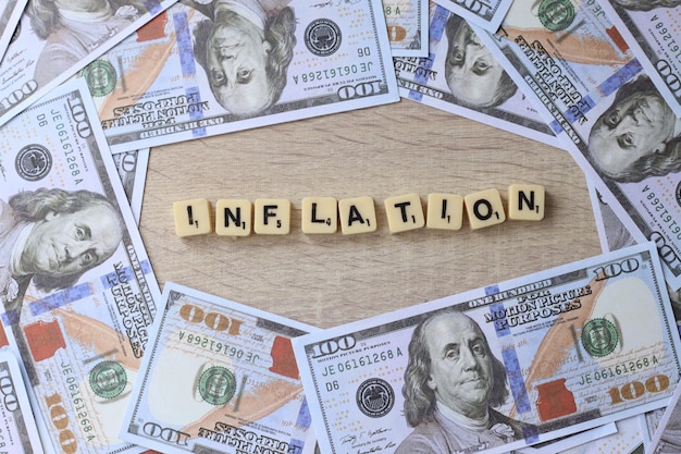 Inflationswörter auf Holzblöcken, umgeben von US-Dollar-Scheinen. Geschäfts- und Finanzkonzept