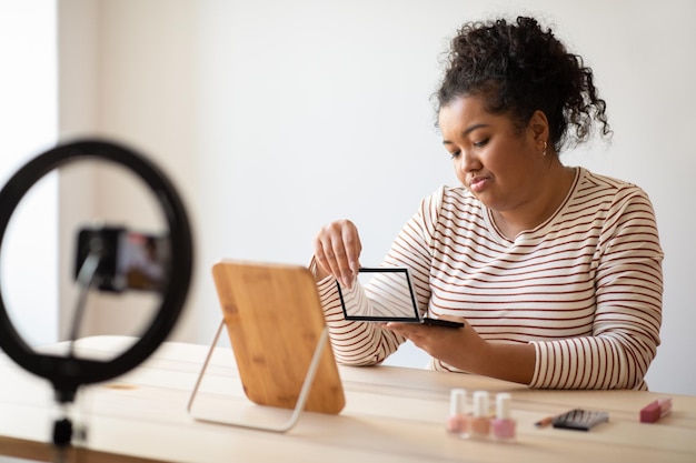 Influencer de belleza decepcionado revisando la paleta de sombras de ojos que se transmite desde su casa