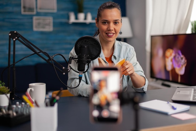 Influencer, der eine gelbe buchrezension für den social-media-kanal aufzeichnet. ersteller von fraueninhalten, der produktempfehlungen für online-vlog im heimstudio mit mikrofon und laptop präsentiert.