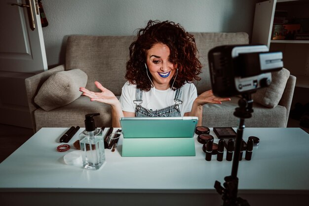 Influencer femenina sonriente con lápiz labial azul durante el rodaje