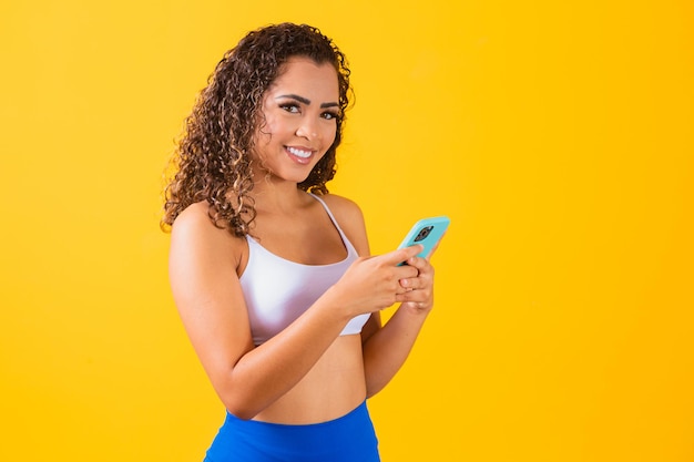 Influencer-Frau im Fitness-Outfit mit Handy auf gelbem Hintergrund