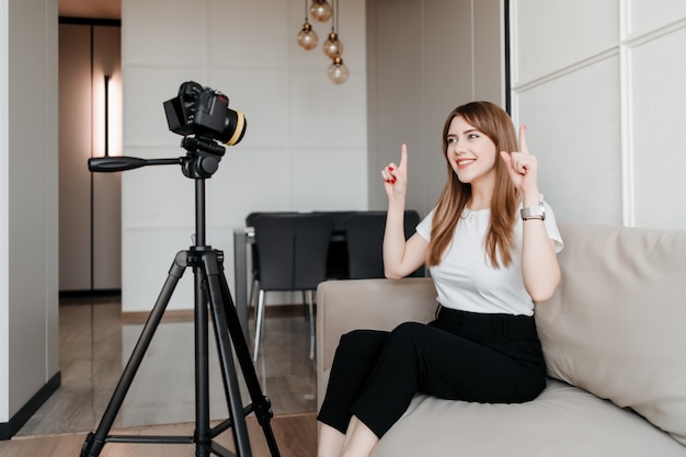 Influencer mujer haciendo video para vlog señalando con el dedo sentado en su casa en el sofá