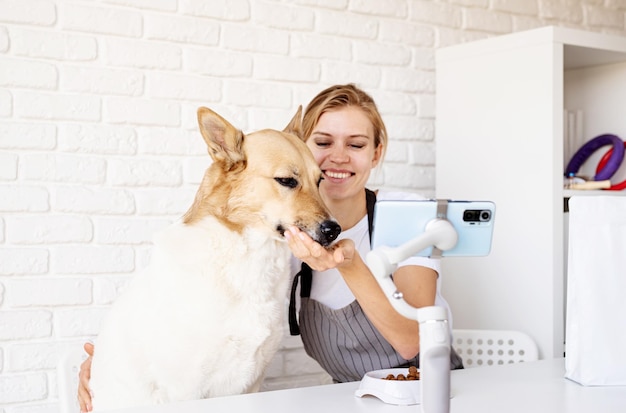 Influenciador de blogueiro jovem sorridente em casa com seu cachorro de raça mista mulher falando sobre comida de cachorro olhando para a câmera falando fazendo videochamada videoconferência blog de estilo de vida vlog