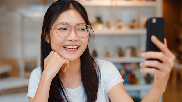 Influenciador de mulheres asiáticas amigáveis do blogueiro acenando com a mão fazendo videochamada em um café noturno