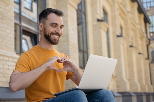 Influenciador de sucesso usando a comunicação do laptop online homem bonito e sorridente fazendo videochamada