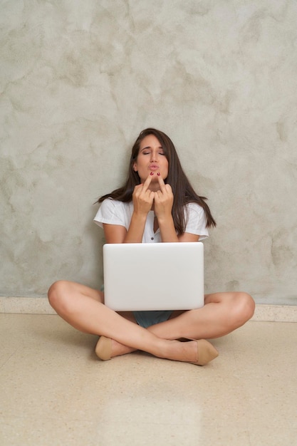 Influenciador de teletrabalho sentado no chão levantando o dedo, foda-se, beije os lábios