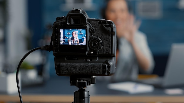 Influenciador de filmación de cámara moderna hablando con la audiencia. Popular creador de contenido de medios sociales grabando vlog para plataformas de intercambio de videos en Internet mientras está sentado en el escritorio del estudio. De cerca