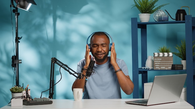 Influenciador haciendo revisión de producto de auriculares inalámbricos mientras graba video en la cámara. Bloguero de redes sociales revisando auriculares en busca de sonidos y música en el canal de vlog. Hombre filmando en estudio