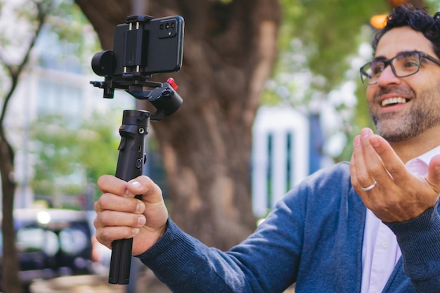 Influenciador latino de meia-idade usando um gimbal sem fio para gravar de seu telefone celular