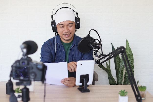 Influenciador de vlogger masculino asiático en auriculares graba blog de video en teléfono inteligente en casa