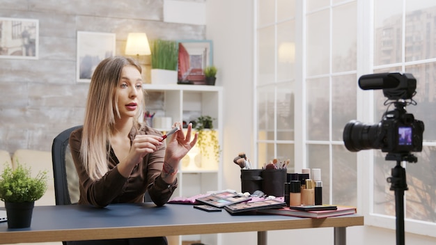Influenciadora atraente gravando um vídeo sobre pincel de maquiagem. Vlogger de cosméticos.