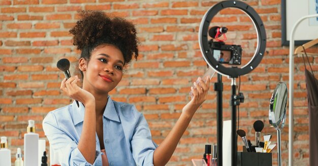 Foto influenciadora feminina filma streaming ao vivo de vlog revisão de vídeo maquiagem crucial mídia social ou blog jovem feliz com iluminação de estúdio de cosméticos para sessão de gravação de marketing transmitida on-line