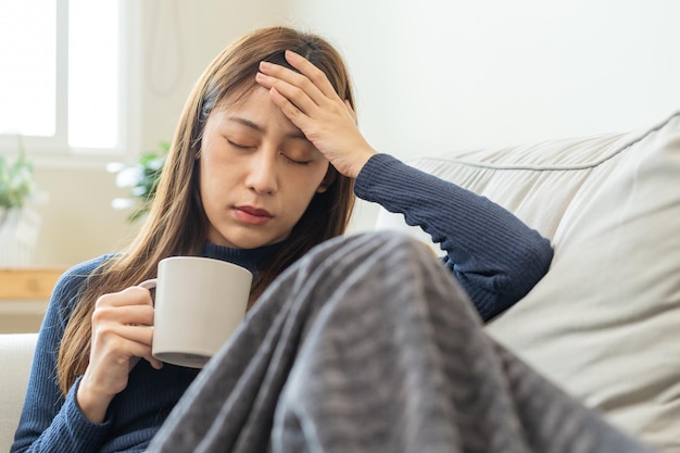 Influenza enferma mujer joven asiática dolor de cabeza tiene fiebre gripe y verifica la temperatura corporal siente enfermedad sentada en el sofá cama en casa Persona de atención médica en virus covid19