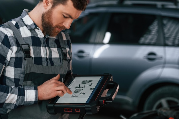 La información gráfica está en la tableta. El hombre en uniforme está trabajando en el salón del automóvil.