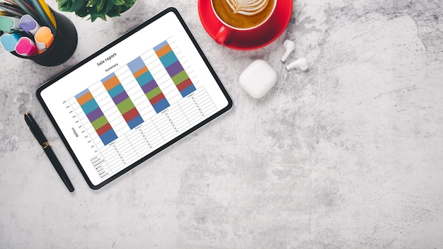 Un informe de ventas profesional en una tableta con gráficos de barras coloridas una taza de café roja y suministros de oficina en una superficie de mármol