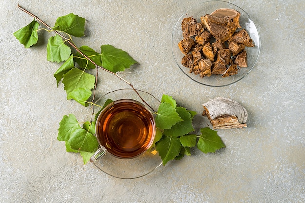 Infusão curativa de cogumelos de bétula chaga em copos de vidro e pedaços de chaga em uma mesa de madeira