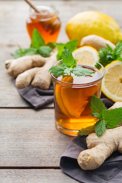 Infusão de bebida quente em copo para gripe fria nos dias de outono. xícara de chá de gengibre com hortelã, limão e mel em uma mesa de madeira