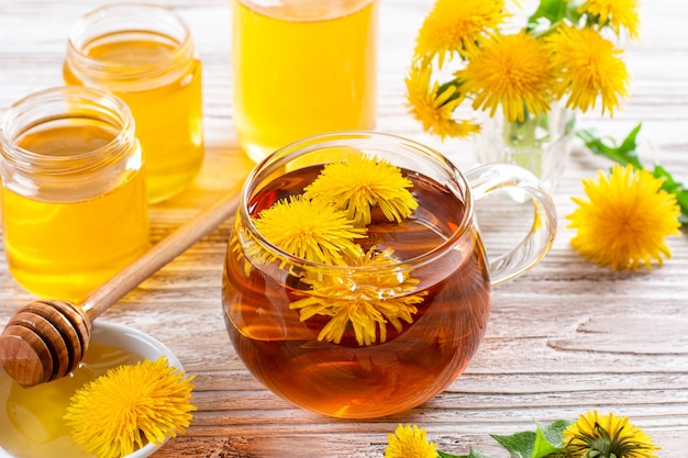 Infusión de té de hierbas de hojas frescas de diente de león, con flores amarillas y miel en la mesa de madera blanca