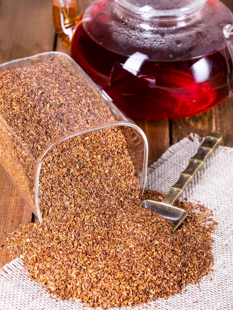 Infusor con hojas secas de rooibos en primer plano de la mesa de madera gris