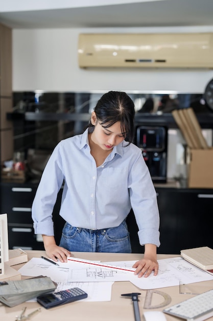 Foto ingeniera arquitecta asiática mujeres trabajando en el diseño de un nuevo proyecto sobre el modelo de construcción y el plan arquitectónico de construcción mientras usa la regla para comprobar y dibujar la arquitectura en el plano en la oficina