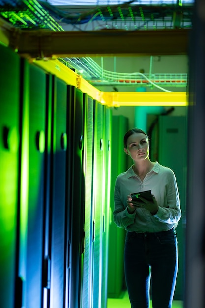 Ingeniera caucásica que usa tableta digital mientras inspecciona la sala de servidores de computadoras. concepto de gestión y mantenimiento del servidor de bases de datos