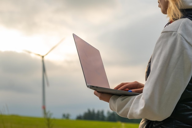 Ingeniera comprobando el trabajo de estabilidad del molino de viento con una computadora portátil en el campo a la luz del sol verde e