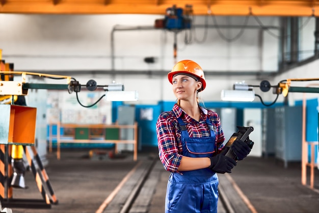 Ingeniera industrial con casco trabajando en la fábrica con controlador industrial