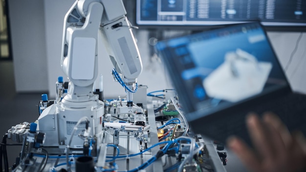 Ingeniera negra que usa una computadora portátil para programar un brazo robótico en la fábrica avanzada futurista Tecnología de nueva generación en la industria de fabricación automática