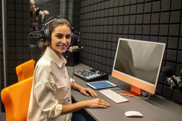 Una ingeniera de sonido sonriente sentada en el escritorio mirando hacia adelante