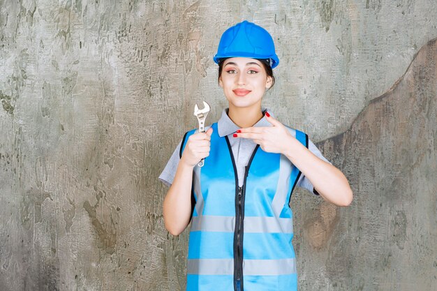 Ingeniera en uniforme azul y casco sosteniendo una llave metálica.