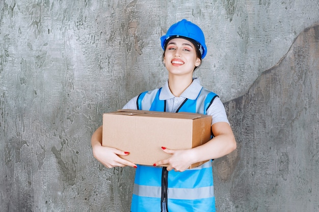 Ingeniera en uniforme azul y casco sosteniendo un paquete de cartón