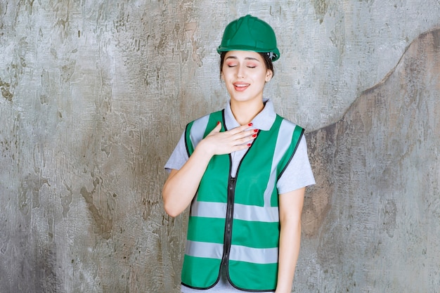 Ingeniera en uniforme verde y casco sintiendo gratitud.