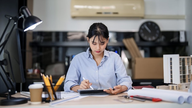 Foto ingenieras arquitectas asiáticas mujeres que trabajan para comprobar sobre el dibujo del plan de arquitectura en la tableta digital mientras son creativas para diseñar un nuevo proyecto sobre el modelo de construcción y el plan arquitectónico de construcción