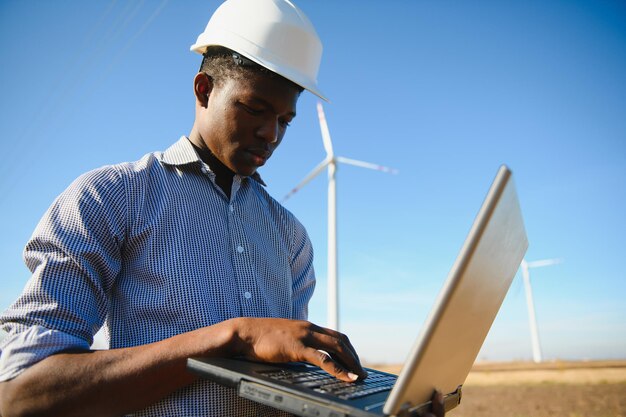 Ingeniero africano de pie y portátil con aerogenerador