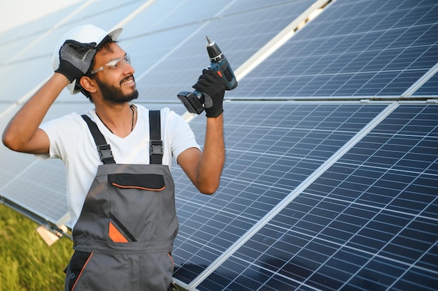 Ingeniero árabe en casco y mono marrón comprobando la resistencia en paneles solares al aire libre hombre indio trabajando en la estación
