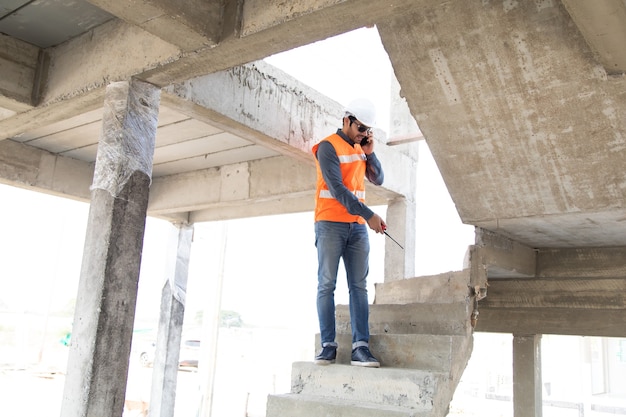 Ingeniero y arquitecto que trabaja en el sitio de construcción con plano. Electricista hispano trabajando y buscando planos en el sitio de construcción de una casa nueva.