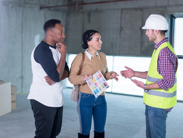 ingeniero arquitecto que usa una tableta mientras muestra los planes de diseño de la casa a una joven pareja multiétnica en el sitio de construcción