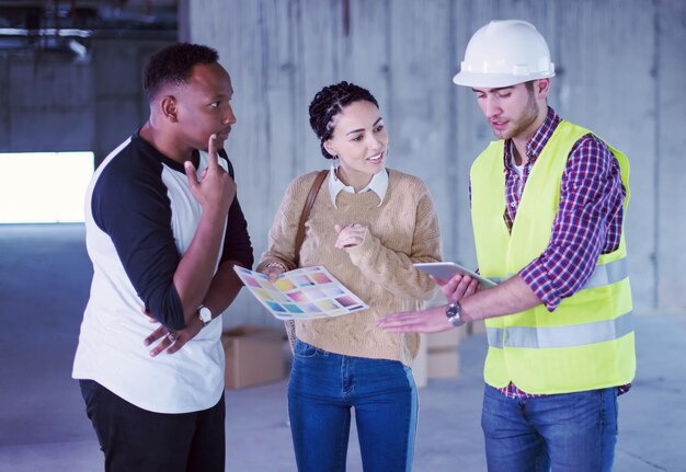 ingeniero arquitecto que usa una tableta mientras muestra los planes de diseño de la casa a una joven pareja multiétnica en el sitio de construcción