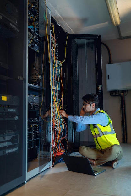 Ingeniero asiático con computadora portátil hablando por teléfono inteligente mientras inspecciona la sala de servidores de computadoras. concepto de gestión y mantenimiento del servidor de bases de datos